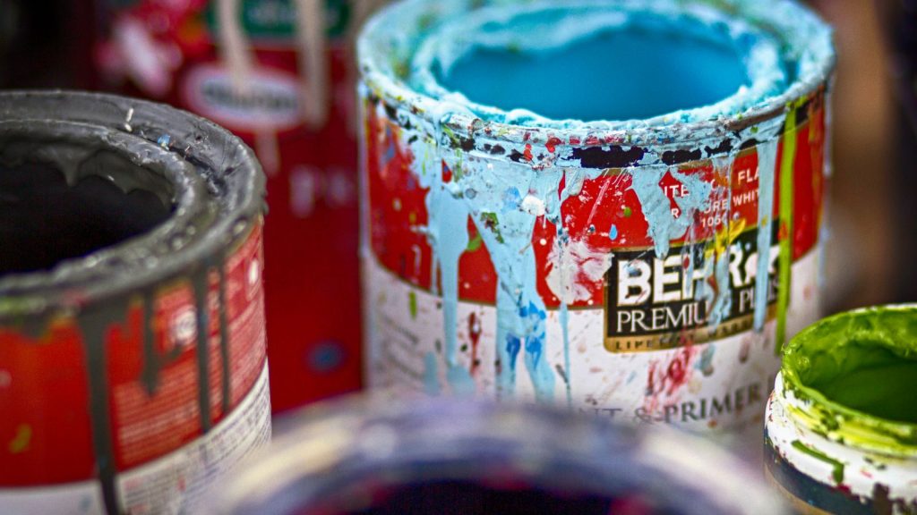 Open tins of used leftover paint with colour splashes on a workshop surface, illustrating how to dispose of paint when moving out