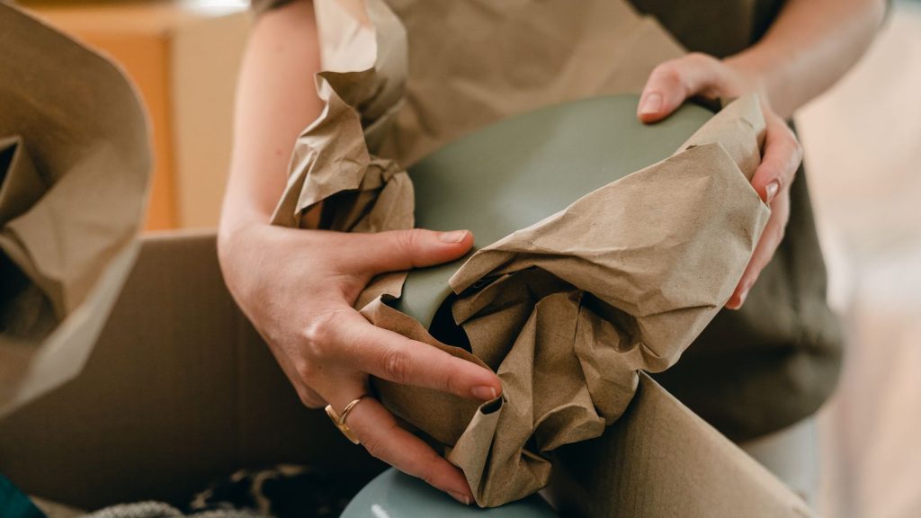 Person wrapping fragile kitchen items in plain packing paper while preparing for a house move